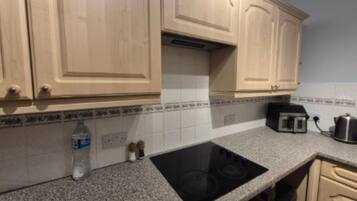 A kitchen with granite countertops, a black induction cooktop, wooden cabinets, and a coffee maker.