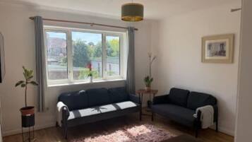 A living room with a sofa, a small table, a potted plant, and a window with curtains.