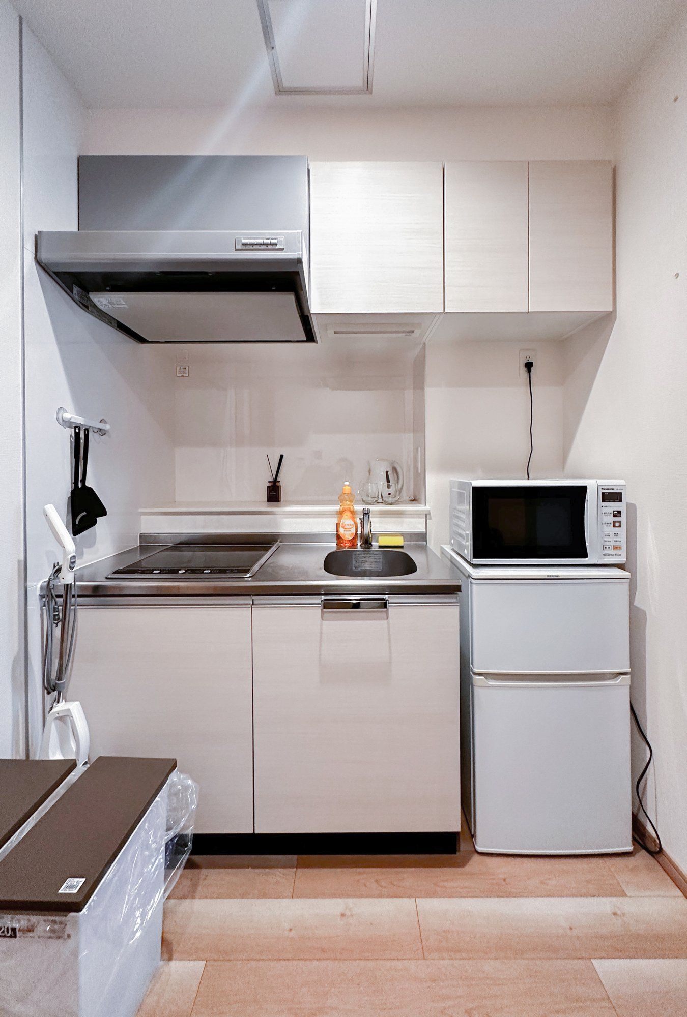 A compact kitchen with white cabinets, a stainless steel range hood, a microwave, and a small sink.