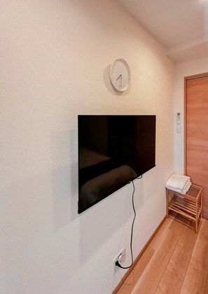 A room with a mounted TV on the wall, a wooden floor, and a door. - HANASTAY CHUO KOKAN 503 (Osaka)