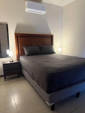 Ein Schlafzimmer mit Bett, Nachttisch, Lampe und Klimaanlage.
