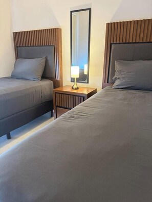 A hotel room with two beds, a nightstand, and a mirror.