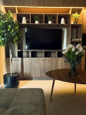 Ein modernes Wohnzimmer mit einem Flachbildfernseher, Holzregalen, einer Topfpflanze und einer Blumenvase.