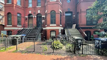 A red brick building with multiple windows and a set of stairs leading to the entrance.