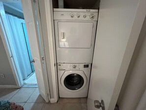 Une petite machine à laver blanche à chargement frontal, installée dans une petite buanderie avec une porte donnant sur une autre pièce.