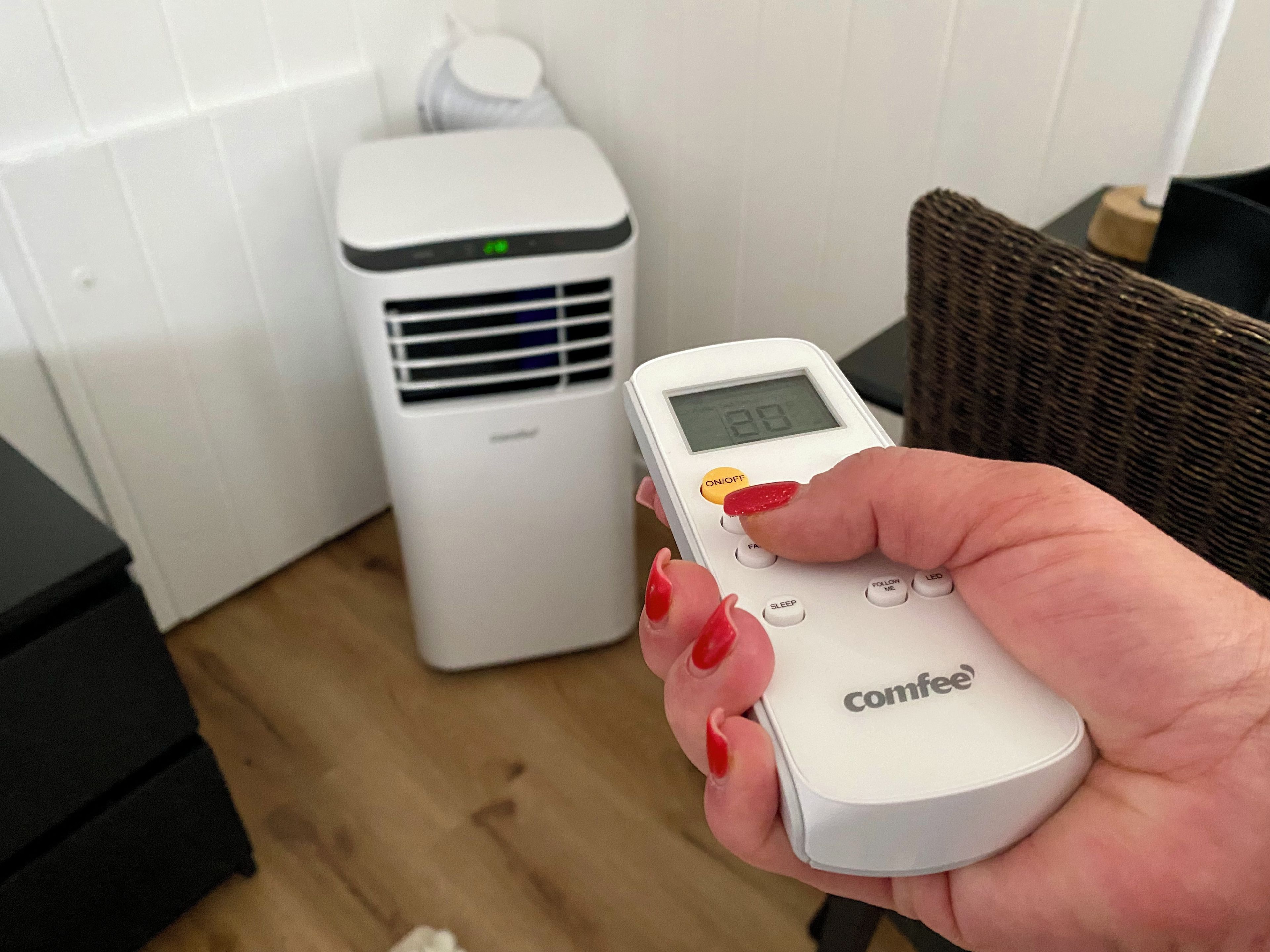 Een hand houdt een witte afstandsbediening met het merk 'Comfee' vast, met een digitaal display.