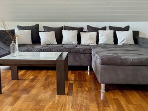 A sectional sofa with multiple cushions, a glass coffee table, and a vase with branches.