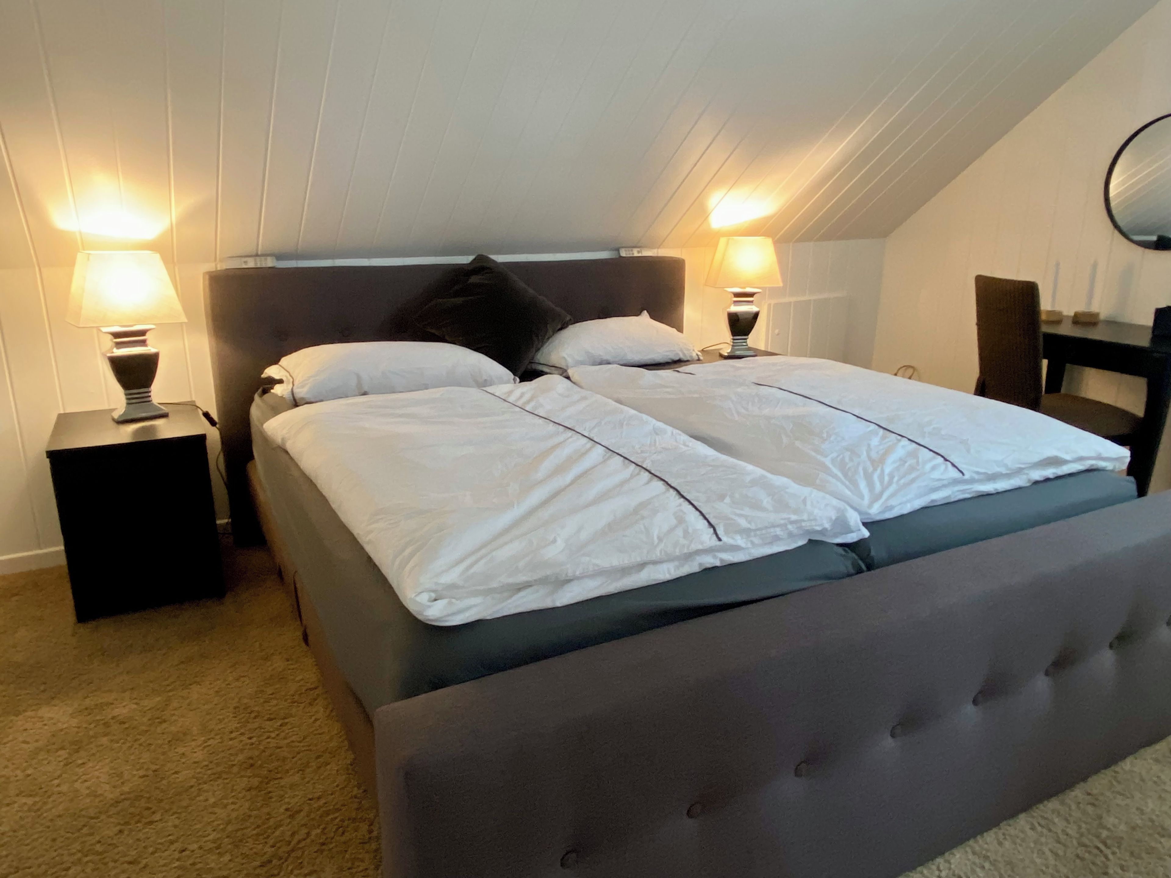 Ein Schlafzimmer mit einem Bett, zwei Nachttischlampen, einem Nachttisch und einem Wandspiegel.