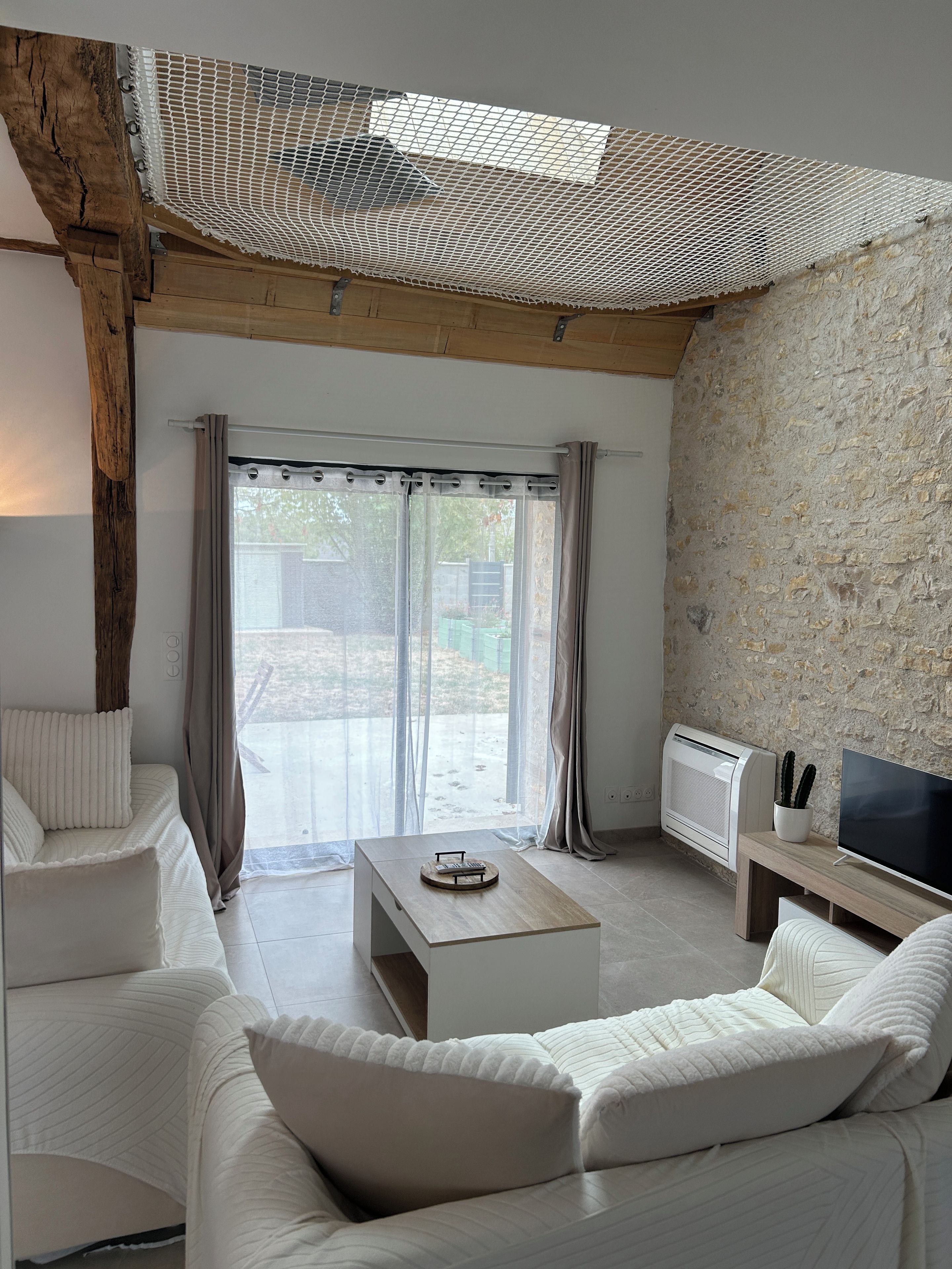 A modern living room with a wooden ceiling, a white sofa, a coffee table, a TV, and a stone wall.