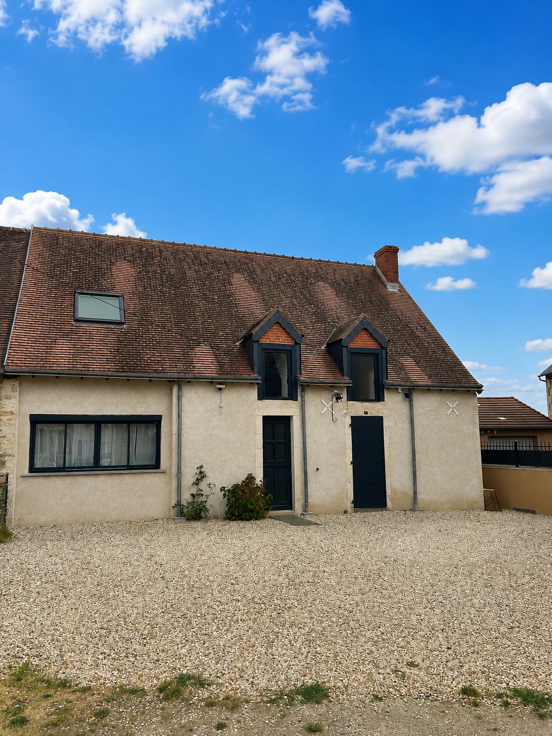 A two-story building with a tiled roof, a gravel driveway, and a small garden area.