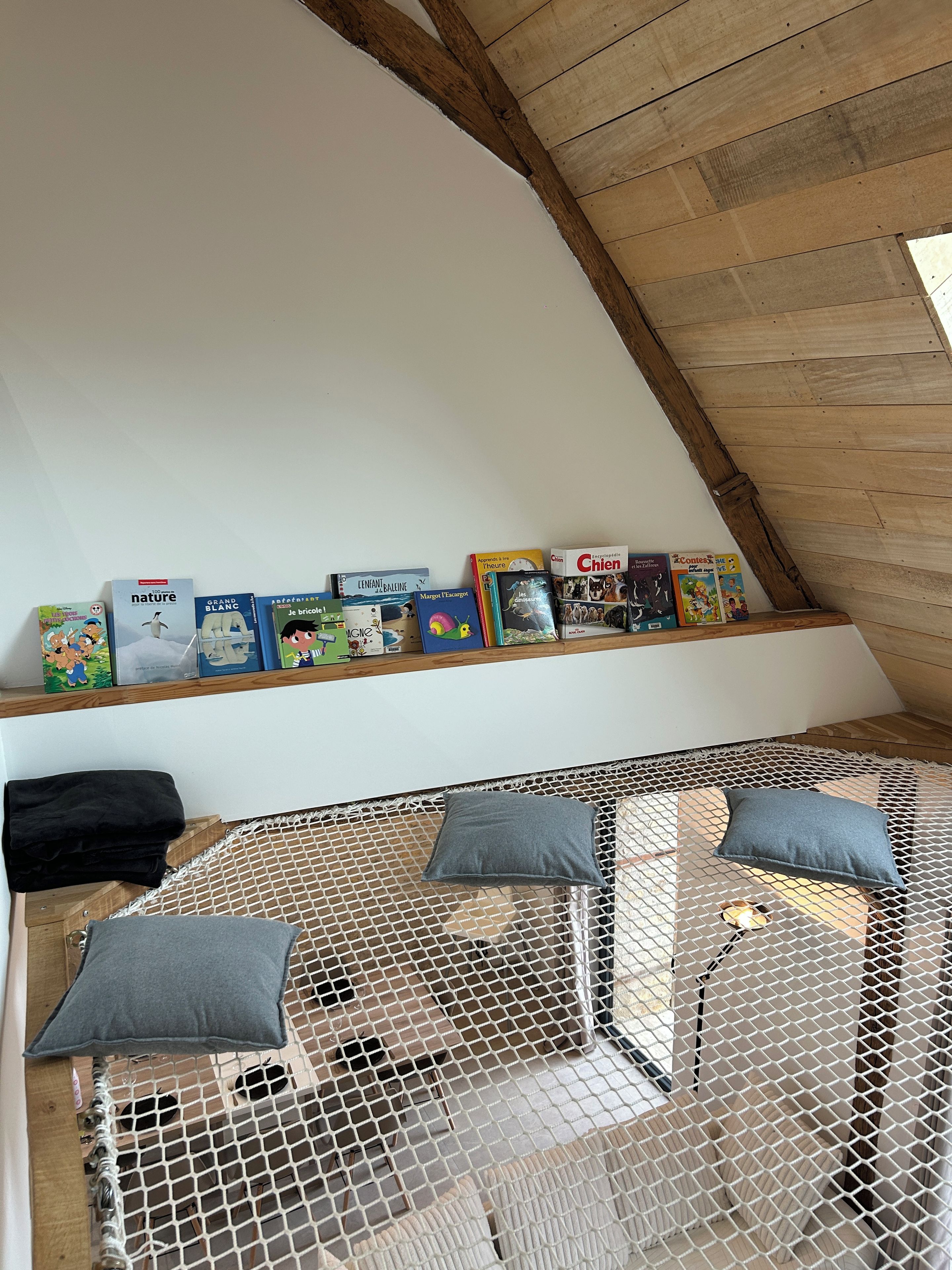Una habitación acogedora en el ático con techo inclinado, una estantería de madera con libros, una cama con dosel de mosquitero y un ventanal.