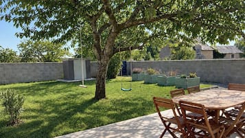 A patio with a table and chairs, surrounded by a grassy area and a tree.