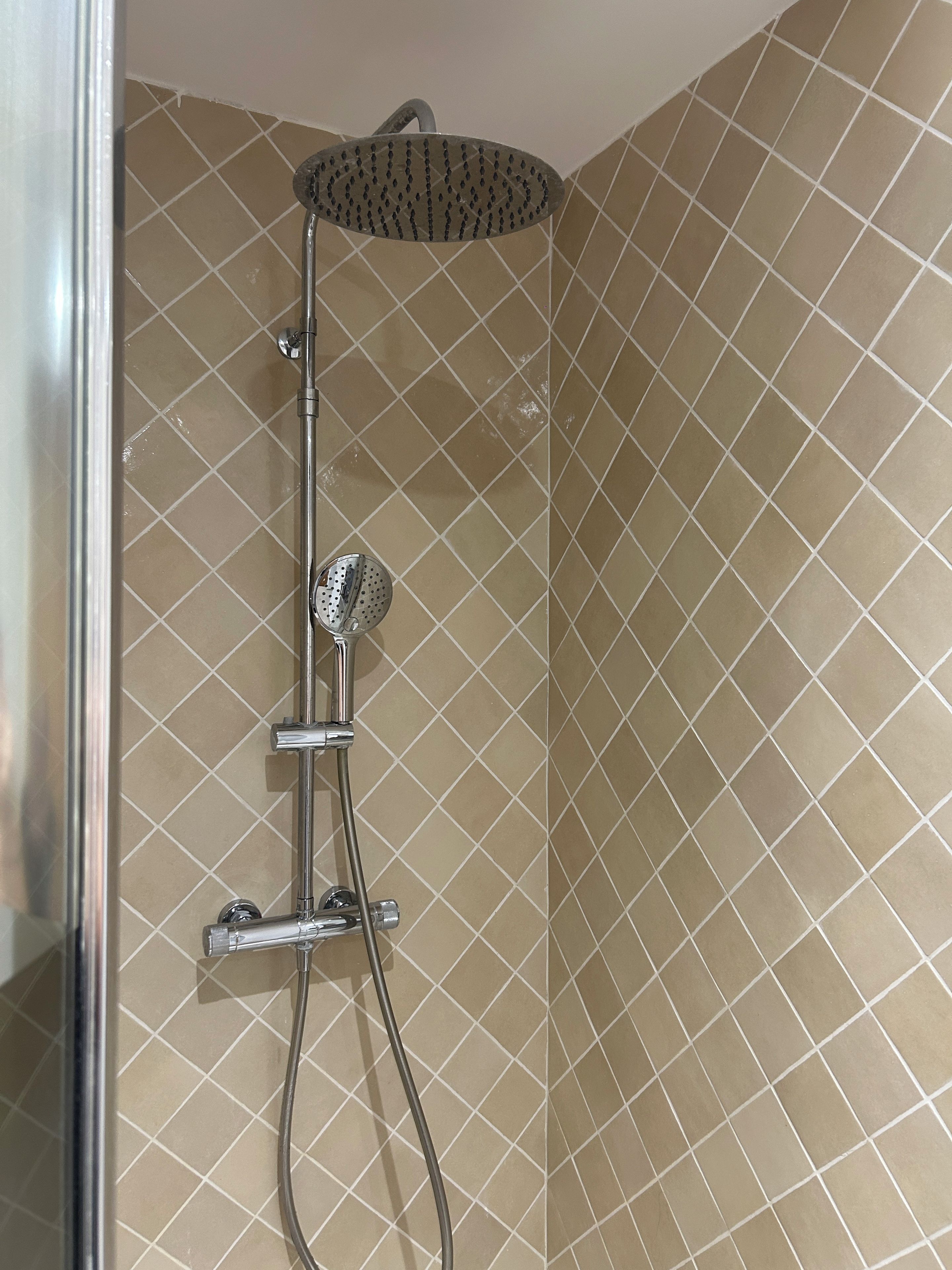 Une douche équipée d’un pommeau de douche à main et d’un accessoire de douche à effet pluie également à main.