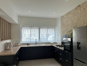 A modern kitchen with a built-in oven, a stainless steel refrigerator, and a window with sheer curtains.