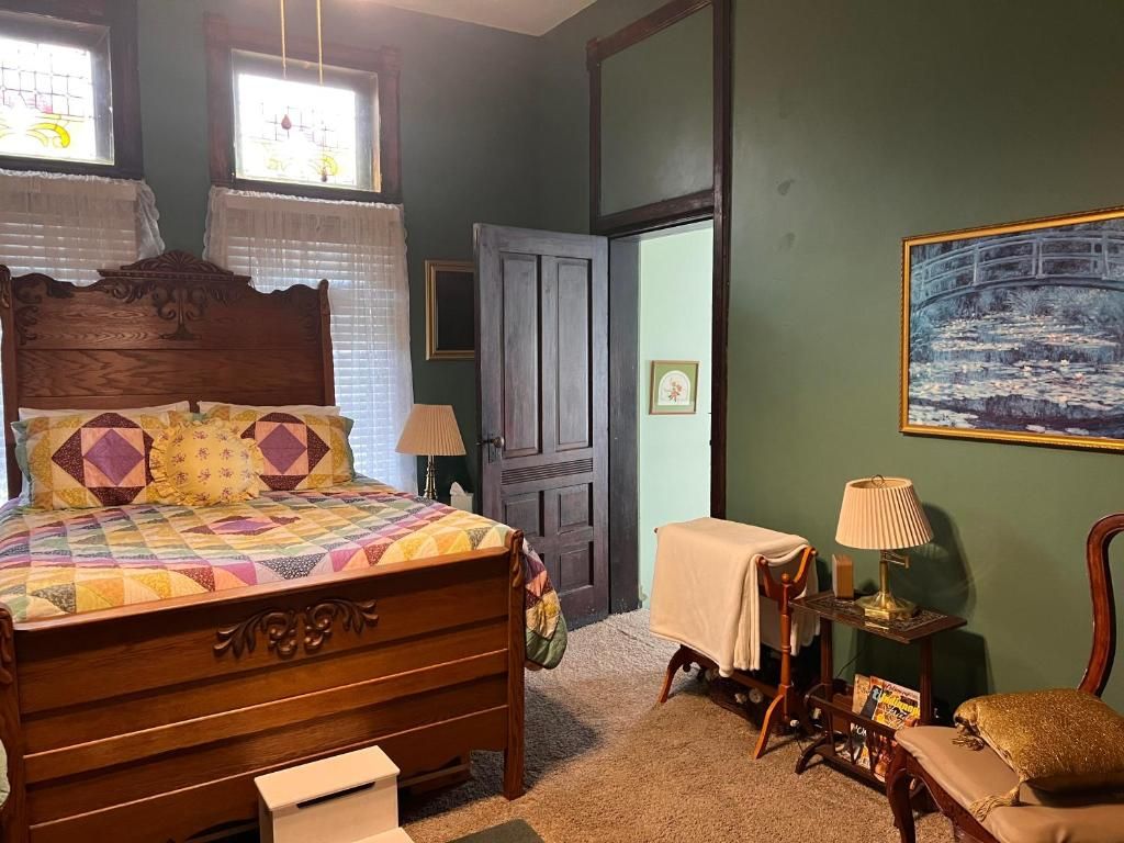A bedroom with a wooden bed, a nightstand, a chair, a painting on the wall, and a door leading to another room.