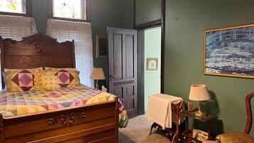 A bedroom with a wooden bed, a nightstand, a chair, a painting on the wall, and a door leading to another room.