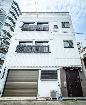A multi-story building with a garage door, air conditioning unit, and a dark-colored door with a sign. - HANASTAY NISHIKI NIPPONBASHI (Osaka)