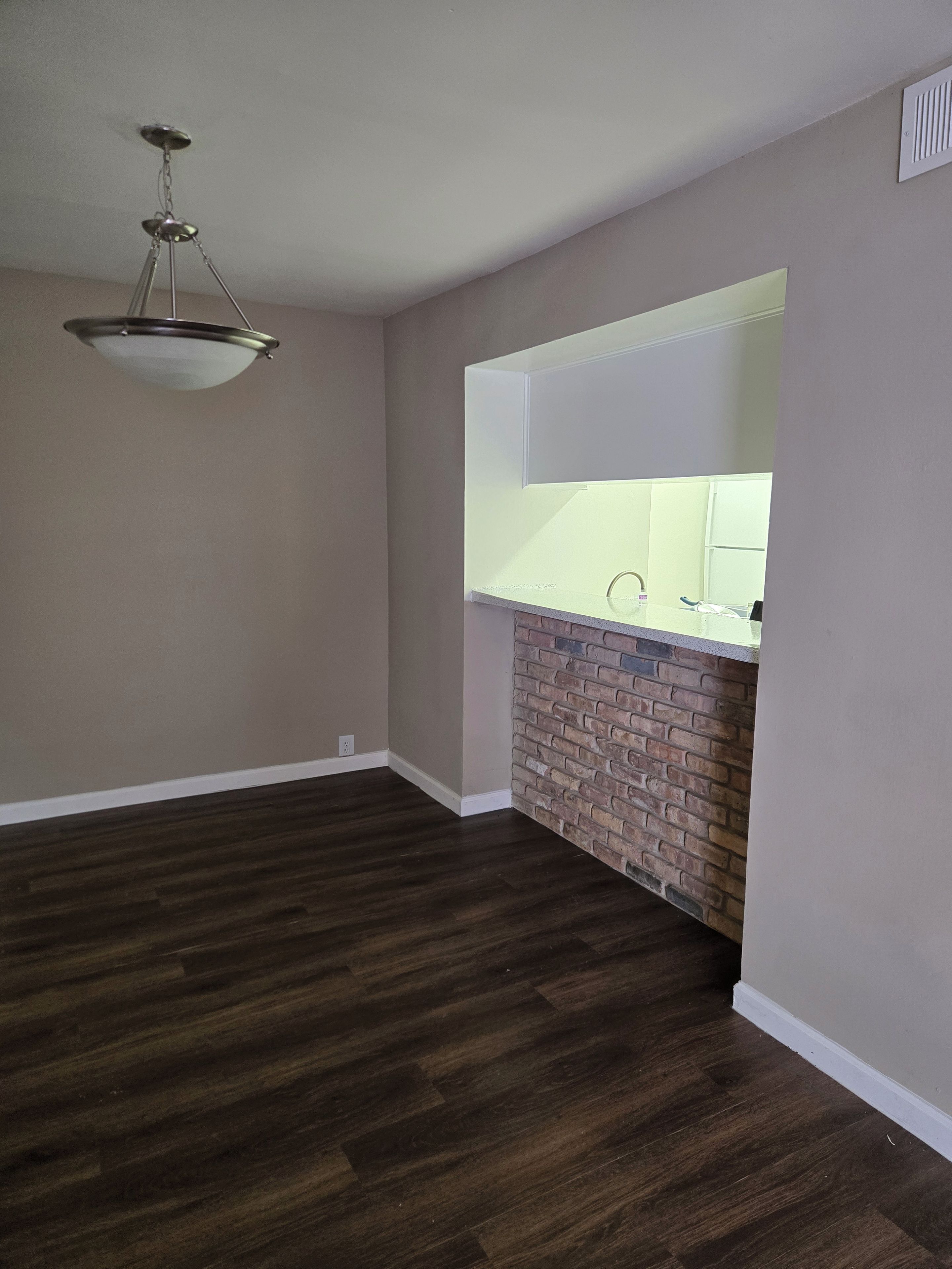 A room with a brick accent wall, a white countertop, and a hanging light fixture.