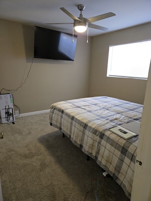 Ein Schlafzimmer mit einem Bett, einem Deckenventilator, einem an der Wand befestigten Fernseher und einem Fenster.