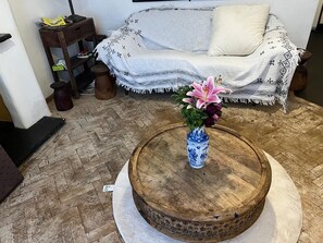Een ronde houten tafel met een bloevas in het midden, een gestreept sofa op de achtergrond en een visgraatvloer.