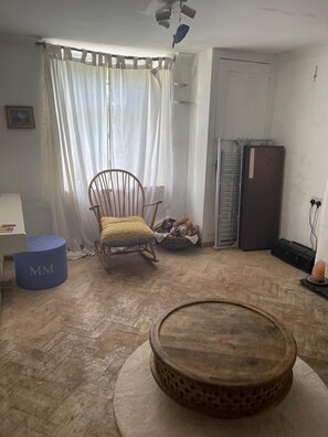 A room with a wooden chair, a small round table, a blue ottoman, a white door, and a refrigerator. - Cosy Garden flat in central Bristol, pet friendly (Bristol)
