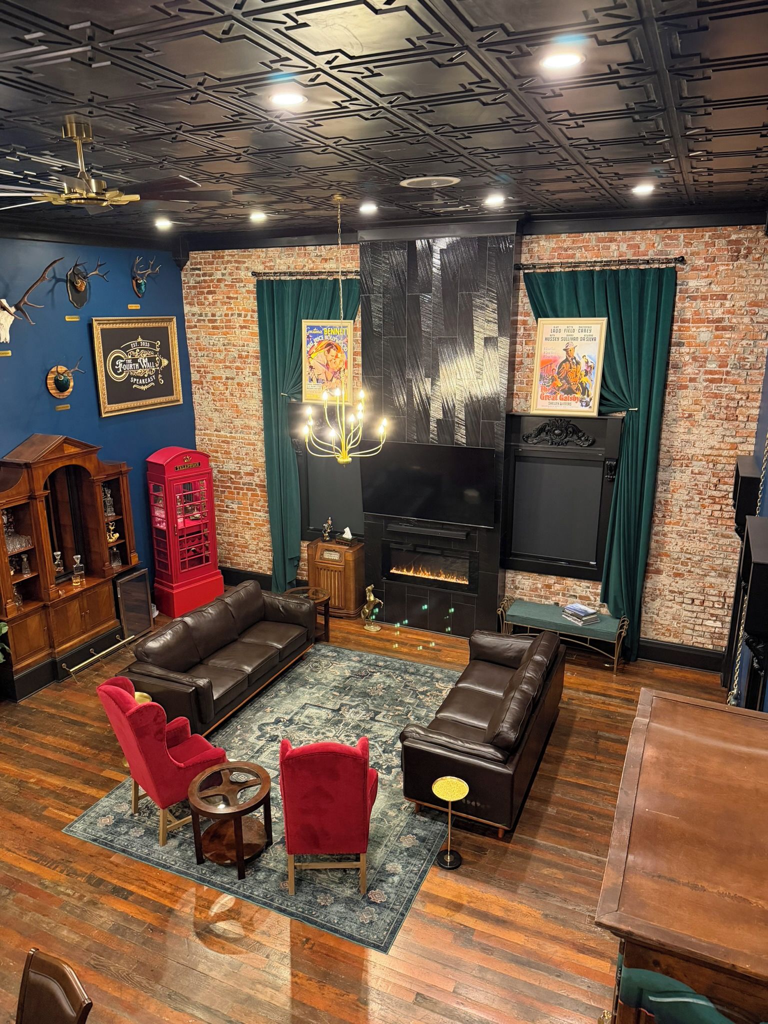 A cozy living room with a fireplace, leather sofas, a red telephone booth, and a brick wall.