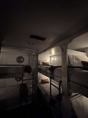 A bunk bed room with numbers on the posts, a circular window, and a light fixture on the wall.