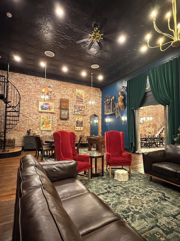 Un coin salon accueillant avec un mur en briques, un ventilateur de plafond et un rideau vert.