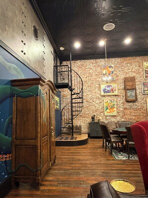 A room with a wooden floor, a spiral staircase, a brick wall with vintage posters, a ticket office sign, and a wooden cabinet.