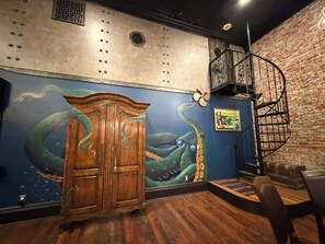 Une pièce avec un meuble en bois, une fresque représentant un poulpe, un mur en briques et un escalier en colimaçon.