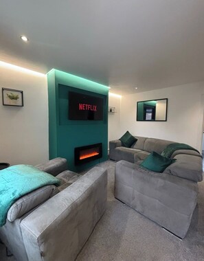 A modern living room with a fireplace, a large flat-screen TV, and two grey sofas with green cushions. - Halton Home Wi-Fi ideal for contractors WA7 (Weston Point)