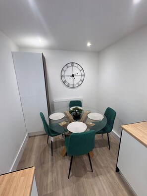 Ein moderner Essbereich mit einem runden Tisch, grünen Stühlen und einer Wanduhr.