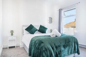 A bedroom with a bed, a nightstand, a lamp, a window, and a view of the outside. - Contractor • 3 Bed Home • Street Parking • Wi-Fi (Halton)