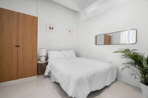 A bedroom with a bed, a wardrobe, a bedside table, a lamp, a mirror, and a potted plant. - Casa San Rafael Apt 3 | Cozy Corner for Two @ SJ (San Juan de Puerto Rico)