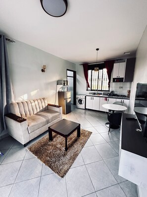 Una sala de estar moderna con un sofá, una mesa de centro y una zona de cocina con electrodomésticos.