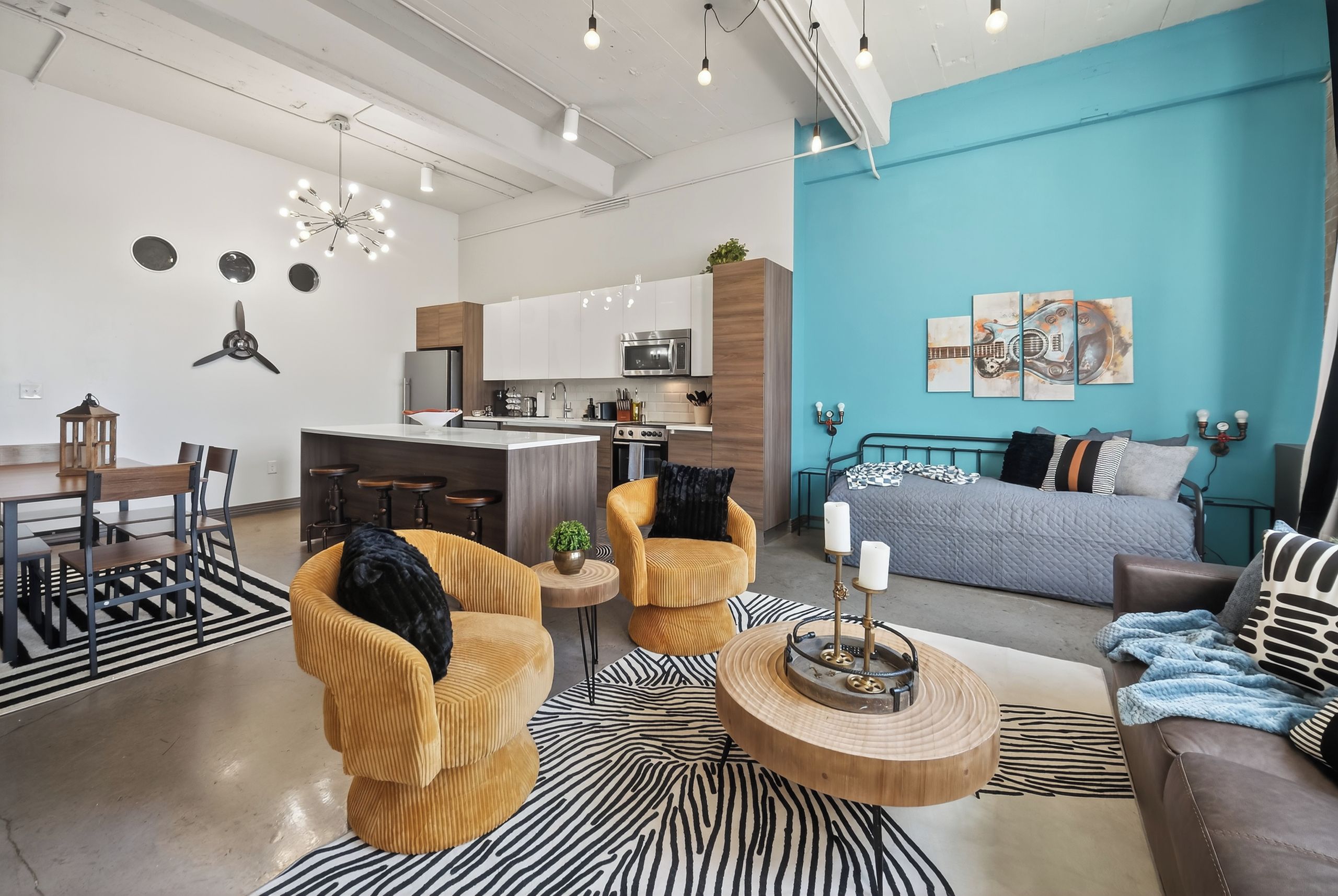 A modern living room with a sofa, armchairs, and a coffee table. There is a kitchen area with cabinets and a dining table.