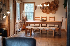 A wooden dining table with chairs and a bench, a chandelier, and a wall decorated with woven baskets.