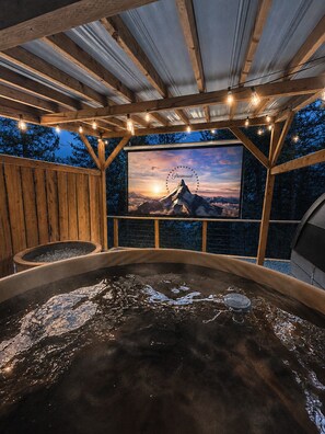 A hot tub with a sunset view, wooden deck, and string lights.