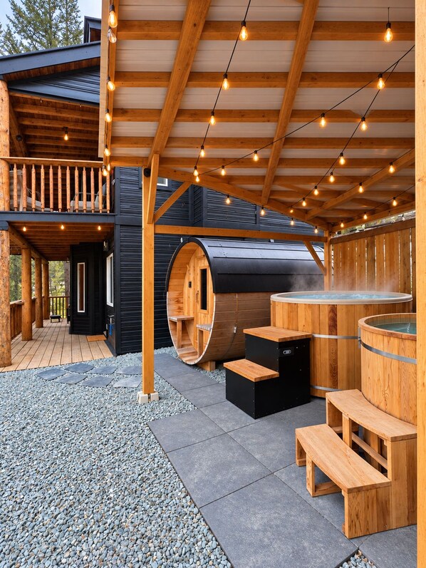 A wooden cabin with a deck, a sauna, and a hot tub.