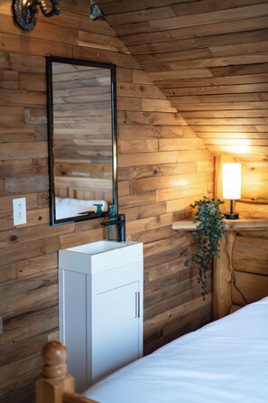 Een kamer met houten lambrisering, een bed, een witte kast, een spiegel, een wandlamp en een plant.