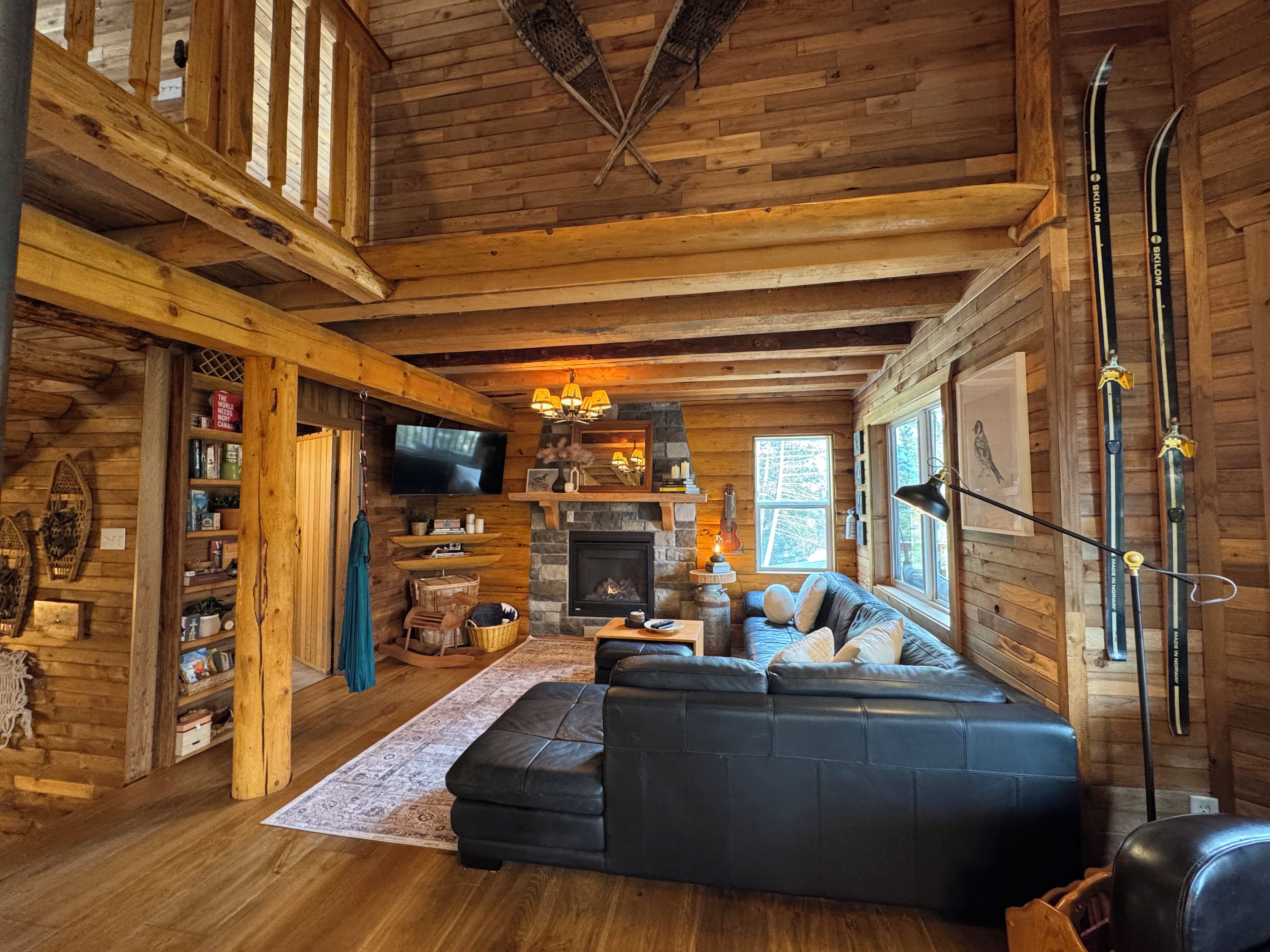 L’intérieur d’un chalet chaleureux, avec une cheminée, des murs en bois, un canapé en cuir et des paires de skis appuyés contre le mur.