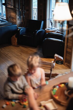 A room with a wooden floor, a black leather sofa, a wooden coffee table, and a lamp on a side table.