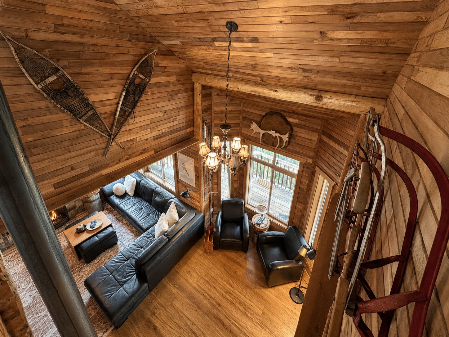 L’intérieur chaleureux d’un chalet avec un plafond en bois, une cheminée, un canapé en cuir noir, une table à manger et un lustre.
