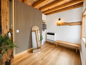 A room with wooden flooring, a bench, a wall-mounted heater, and a mirror reflecting a door. - Snow & Soak | Private Hot Tub, Sauna & Cold Plunge Near Manning Park (Manning Park)