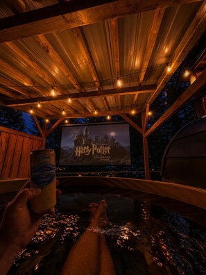 A wooden deck with a large screen displaying a movie poster, surrounded by string lights.