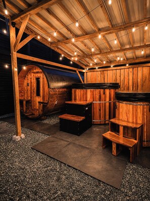 A rustic wooden outdoor seating area with a barrel, wooden steps, and string lights. - Snow & Soak | Private Hot Tub, Sauna & Cold Plunge Near Manning Park (Manning Park)