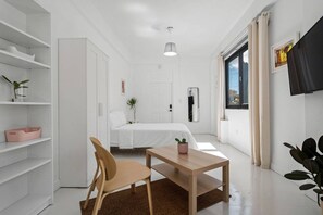 A modern, minimalist bedroom with a bed, a desk, and a chair. There is a TV mounted on the wall and a window with curtains. - San Rafael Apt 5 | Your 1BR Comfort Zone @San Juan (San Juan de Puerto Rico)