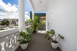 A balcony with white columns, potted plants, and a view of buildings and hills. - San Rafael Apt 5 | Your 1BR Comfort Zone @San Juan (San Juan de Puerto Rico)