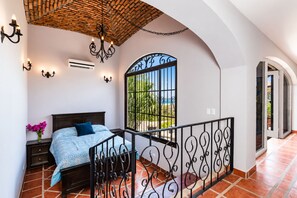 A bedroom with a bed, a nightstand, a vase of flowers, a chandelier, and a view of the outdoors. - Ocean View Villa • Tamarindo 5 min • Walk to Beach (Tamarindo)