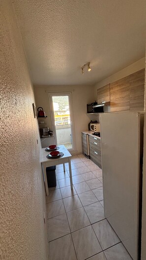 A narrow kitchen with a sliding door leading to a balcony, a microwave, a stove, and a refrigerator. - Cozy apartment with a view of the Paillon garden (Nice)